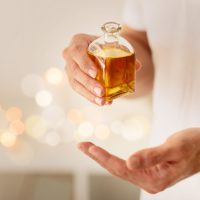 A person is captured holding a glass bottle of golden massage oil, with a bokeh background suggesting a luxurious spa environment